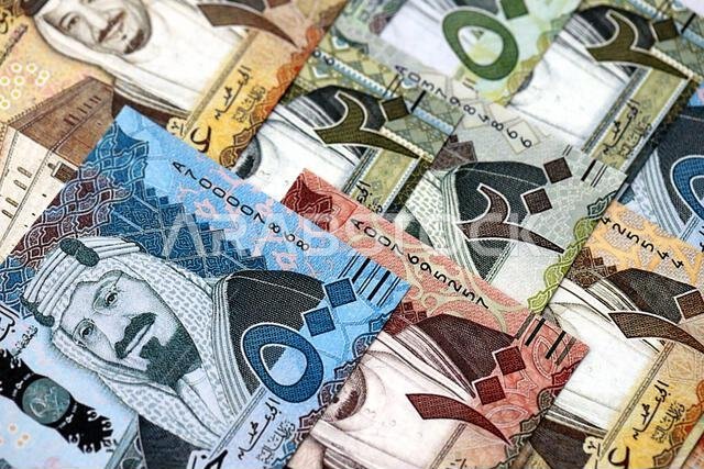 أوراق نقدية من الريال السعودي مكدسة في كومة كبيرة على طاولة، صورة مقرّبة. مفهوم التمويل والأعمال في المملكة العربية السعودية