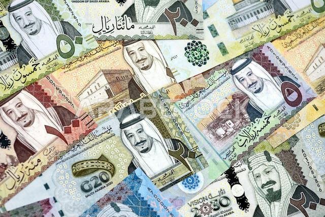 Saudi Arabia riyal money bills banknotes lies in big pile on table close up. Concept of finances and business in Saudi Arabia