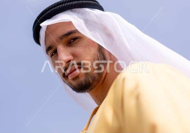 صورة من زاوية منخفضة لرجل عربي في الهواء الطلق يرتدي ملابس عربية تقليدية.