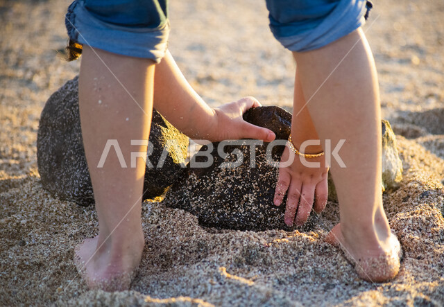 صورة ابداعية ليد طفلة تمسك برمال البحر على شاطئ البحر في المملكة العربية السعودية، اللعب بالرمال، رمال البحر، انشطة ترفيهية على شاطئ البحر، السياحة في السعودية