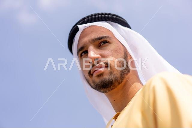 صورة من زاوية منخفضة لرجل عربي في الهواء الطلق يرتدي ملابس عربية تقليدية.