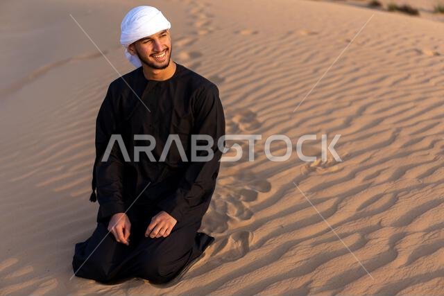 رجل عربي يجلس على الرمال في الصحراء وقت الغروب، مرتدياً الزي العربي التقليدي. صورة عالية الجودة