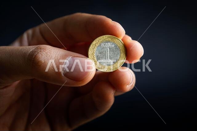 صورة مقربة ليد تحمل عملة معدنية سعودية من فئة ريال واحد، تظهر تفاصيل عربية دقيقة وملمسًا معدنيًا.