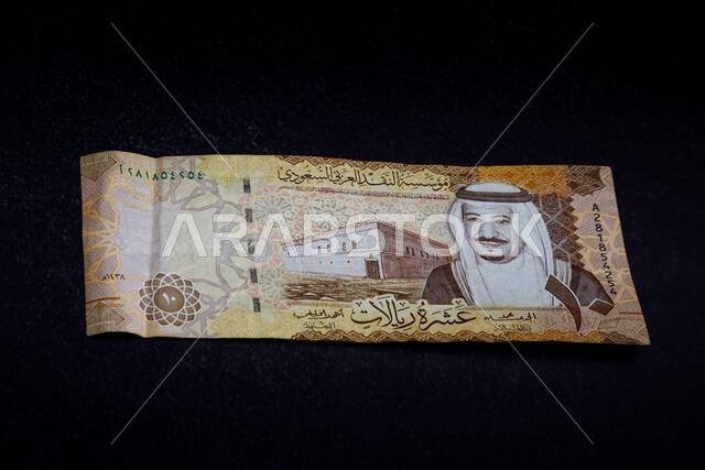 أوراق نقدية من فئة الريال السعودي على خلفية داكنة تحمل صور الملك سلمان ومعالم وطنية سعودية. أوراق نقدية من فئة الريال السعودي على خلفية داكنة تحمل صور الملك سلمان ومعالم وطنية سعودية.
