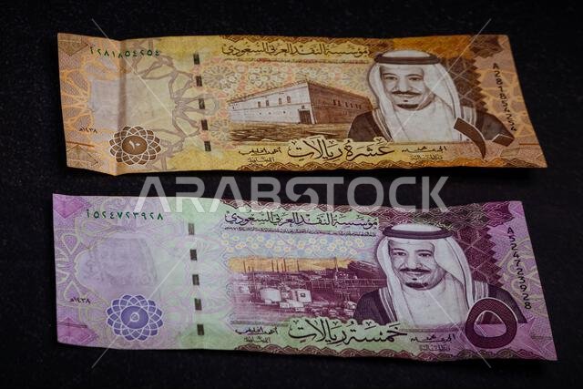 أوراق نقدية من فئة الريال السعودي على خلفية داكنة تحمل صور الملك سلمان ومعالم وطنية سعودية.