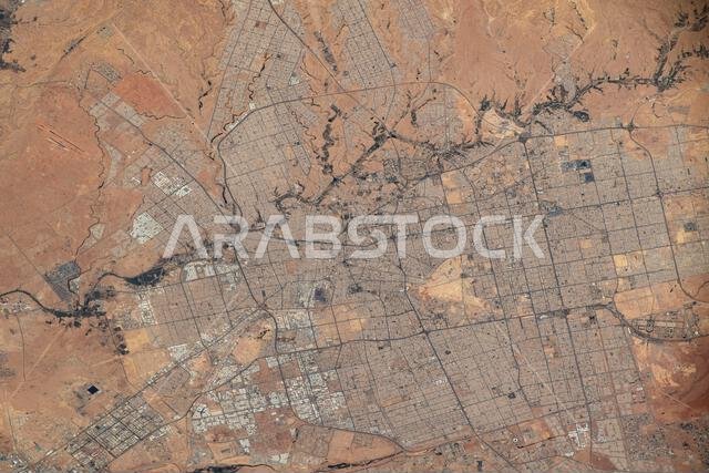 Riyadh, the capital and largest city of Saudi Arabia.  A photograph taken from the International Space Station on 20 April 2023. Riyadh is situated in the central region of Saudi Arabia and serves as the nation's legislative and financial hub. The urban area appears grey, contrasting sharply with the pinkish-tan bare desert ground surrounding the city. The city has a distinct grid pattern for its streets and isolated patches of dark green vegetation are visible.  An optimised version of an origi