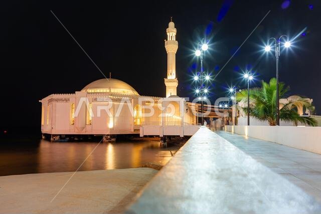 Jeddah, Saudi Arabia - December 23, 2025: A tranquil night scene of a white Al Rahma Mosque, Floating Mosque, on stilts by the water, connected to a l
