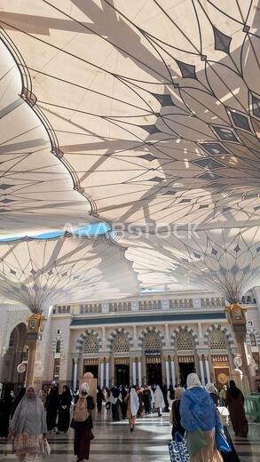 المدينة المنورة، المملكة العربية السعودية - 5 مارس 2024: الحجاج يسيرون إلى المسجد النبوي الشريف تحت مظلة عملاقة استعدادًا للصلاة.