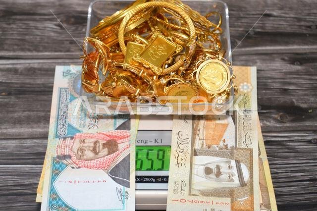 Cairo, Egypt, January 9 2026: SAR Saudi Arabian riyals money and a Pile stack of gold on a digital scale in grams, gold bars, sovereigns, bracelets, r