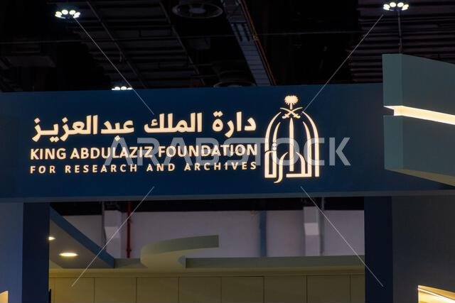 Illuminated sign featuring the logo and bilingual text for the King Abdulaziz Foundation for Research and Archives displayed at an exhibition.