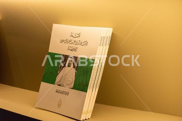 مجموعة من كتب السيرة الذاتية العربية التي تحمل صورة ملك سعودي على غلافها، معروضة على رف.