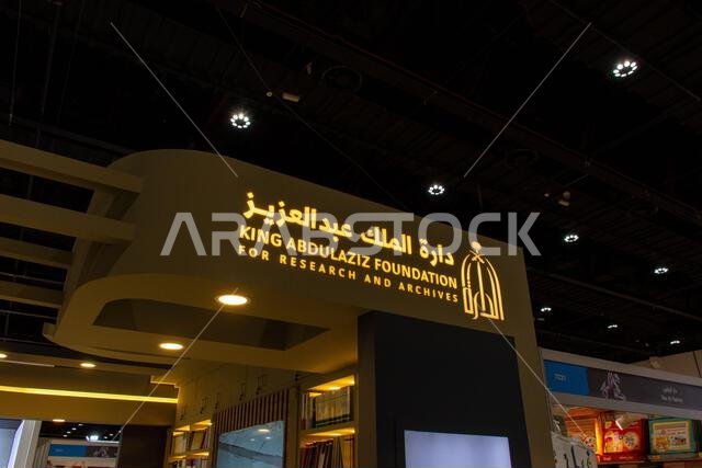 Illuminated sign featuring the logo and bilingual text for the King Abdulaziz Foundation for Research and Archives displayed at an exhibition.
