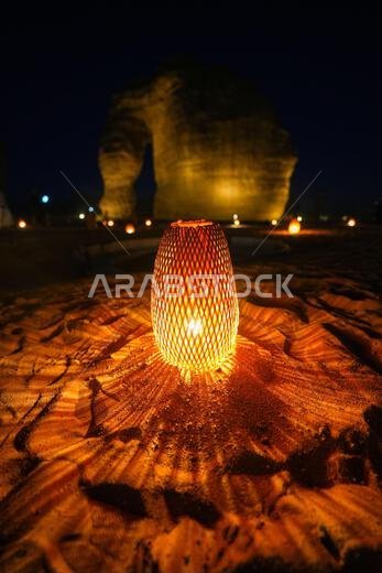 Traditional wicker lantern glowing on the sand at the bottom of Elephant Rock (Jabal Al-Fil) at night in the desert of AlUla, Saudi Arabia