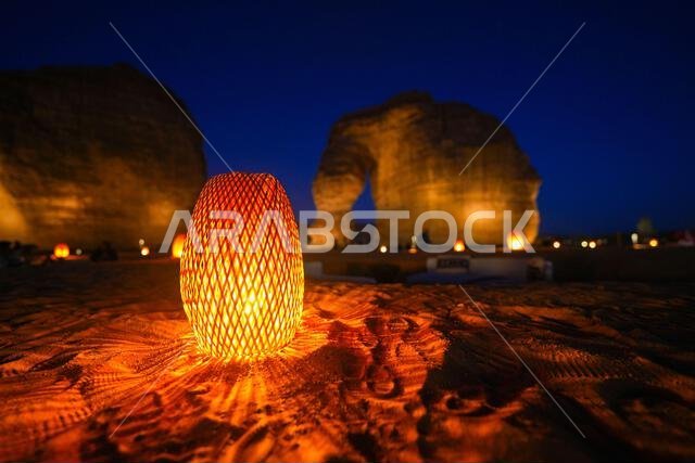 Traditional wicker lantern glowing on the sand at the bottom of Elephant Rock (Jabal Al-Fil) at night in the desert of AlUla, Saudi Arabia Traditional wicker lantern glowing on the sand at the bottom of Elephant Rock (Jabal Al-Fil) at night in the desert of AlUla, Saudi Arabia