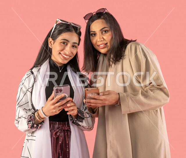 Portrait of two Saudi Arabian Gulf women using a mobile phone, browsing social networking sites, communication and communication, online shopping, using electronic applications, remote work, chat and acquaintance