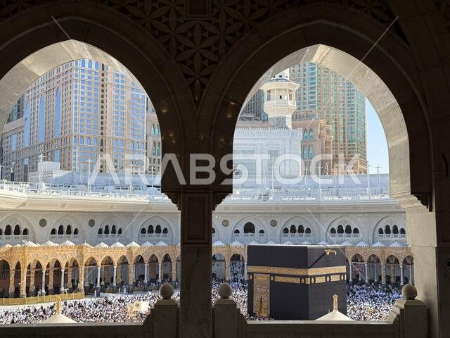 الحجاج يطوفون حول الكعبة المشرفة في المسجد الحرام بمكة المكرمة، محاطين بأقواس المسجد المزخرفة.