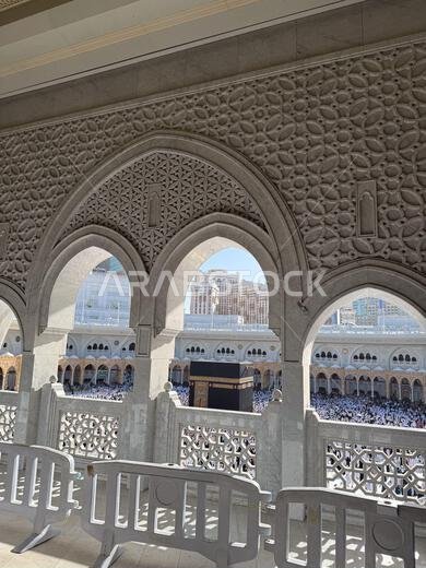 View of the Kaaba and pilgrims at Masjid al-Haram in Mecca through ornate stone arches