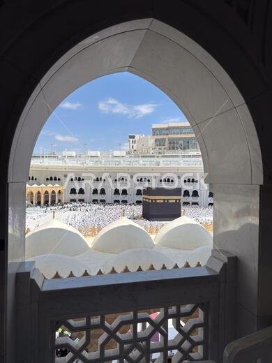 منظر للكعبة والحجاج في المسجد الحرام بمكة المكرمة، مؤطر بنافذة مقوسة