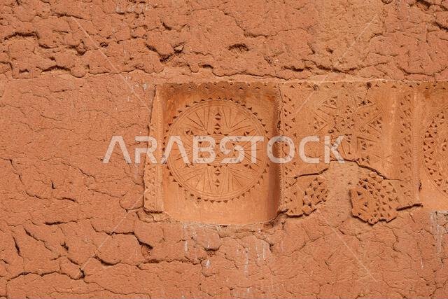 Ancient adobe relief art featuring a circular rosette pattern in Shaqra, Saudi Arabia