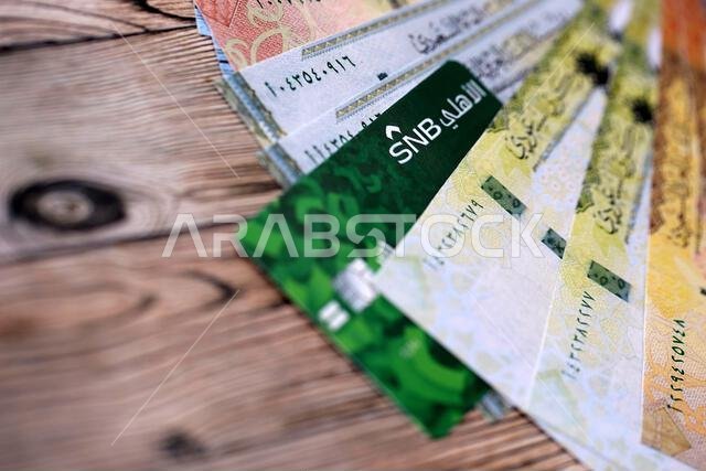 KYIV, UKRAINE - JANUARY 28, 2026 Saudi National Bank card and Saudi riyal money bills on table close up. Saudi National Bank is most popular bank in Saudi Arabia
