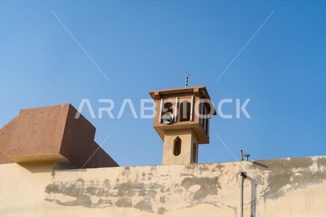 The Masjid Minaret, A slender minaret pierces the twilight sky. A traditional Arabian market building with crenelated walls stands against a rocky hil