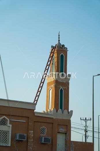 The Masjid Minaret, A slender minaret pierces the twilight sky. A traditional Arabian market building with crenelated walls stands against a rocky hil