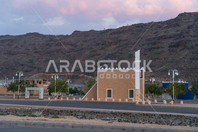 The Masjid Minaret, A slender minaret pierces the twilight sky. A traditional Arabian market building with crenelated walls stands against a rocky hil