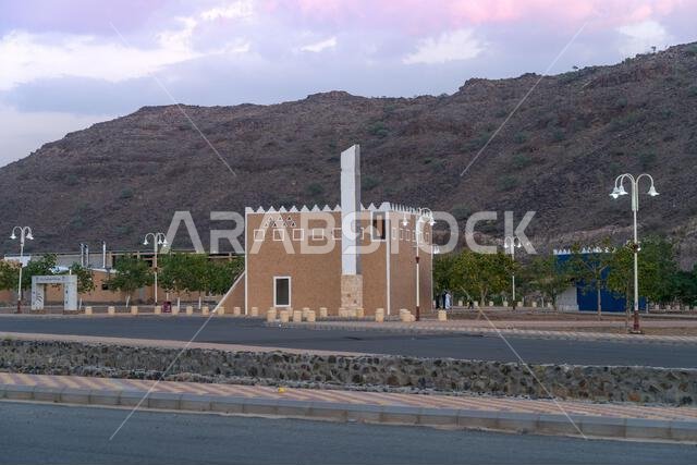 مئذنة المسجد، مئذنة رشيقة تخترق سماء الغسق. مبنى سوق عربي تقليدي ذو جدران مسننة يقف شامخًا على سفح تل صخري.