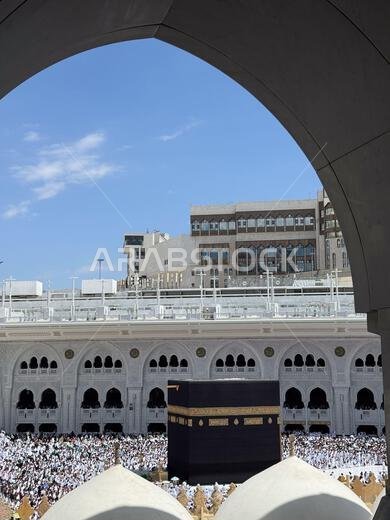 الحجاج يطوفون حول الكعبة المشرفة في المسجد الحرام بمكة المكرمة تحت سماء زرقاء محاطة بقوس
