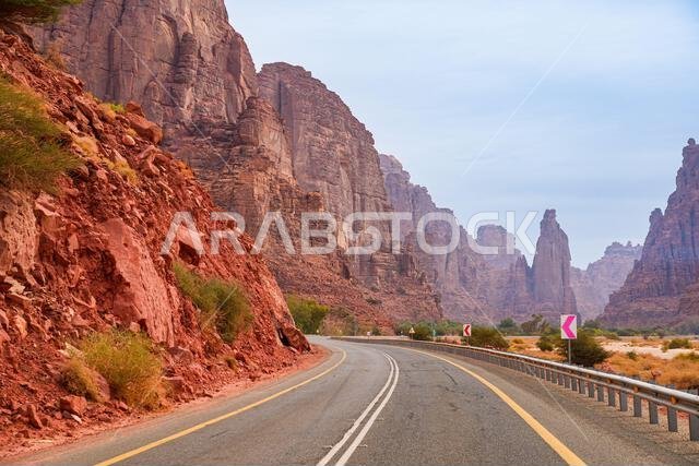 Modern asphalt road winding through the majestic sandstone cliffs of Wadi Al Disah near Tabuk in Saudi Arabia