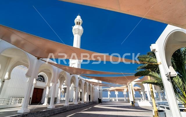 منظر خارجي لمسجد الرحمة في جدة يضم أقواسًا بيضاء تقليدية ومظلات شمسية حديثة تحت سماء زرقاء صافية.
