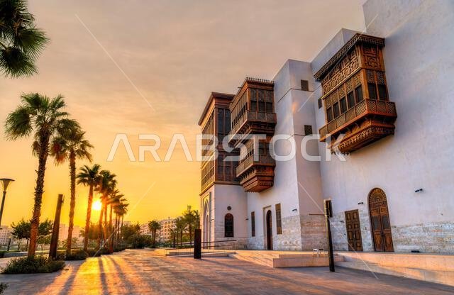 منظر للعمارة التقليدية في ساحة الثقافة بجدة، المملكة العربية السعودية، والتي تتميز بشرفات روشن الخشبية وأشجار النخيل عند غروب الشمس.