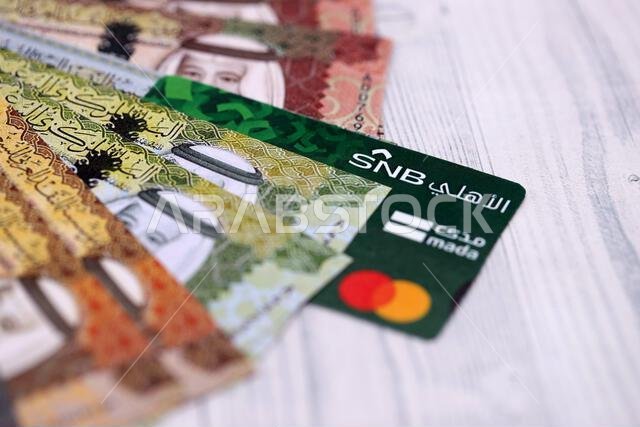 كييف، أوكرانيا - ٢٨ يناير ٢٠٢٦: صورة مقرّبة لبطاقة البنك الوطني السعودي وأوراق نقدية من الريال السعودي على طاولة. يُعدّ البنك الوطني السعودي البنك الأكثر شعبية في المملكة العربية السعودية. كييف، أوكرانيا - ٢٨ يناير ٢٠٢٦: صورة مقرّبة لبطاقة البنك الوطني السعودي وأوراق نقدية من الريال السعودي على طاولة. يُعدّ البنك الوطني السعودي البنك الأكثر شعبية في المملكة العربية السعودية.