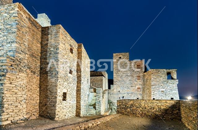 The illuminated stone architecture of the historic Thee Ain Heritage Village at night in Al Bahah, Saudi Arabia.