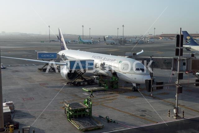 View of King Abdulaziz International Airport in Jeddah, Saudi Arabia, Middle East. Passenger terminal with Saudia airplane under maintenance check