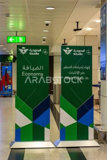 Two green and blue "Economy" and "Web Check-in" signs for Saudia Airlines in Dubai International Airport, UAE.