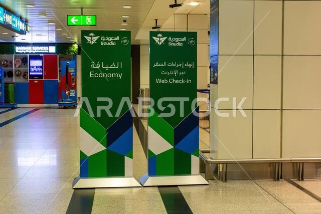 لوحتان خضراوان وزرقاوان تحملان عبارة "الدرجة السياحية" و"تسجيل الوصول عبر الإنترنت" لشركة الخطوط الجوية السعودية في مطار دبي الدولي، الإمارات العربية المتحدة.