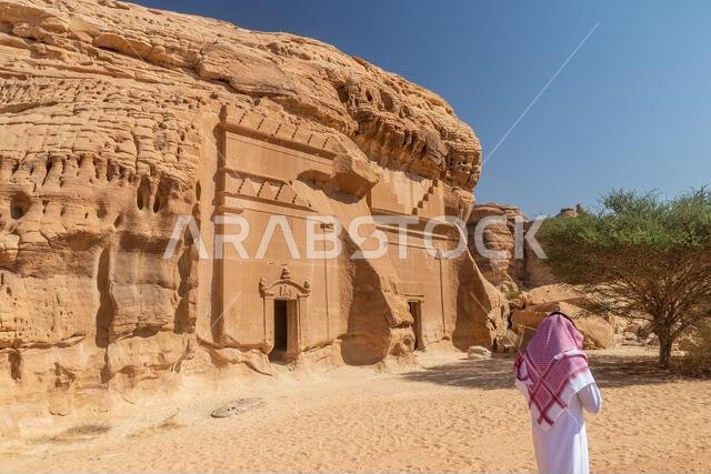 العلا، المملكة العربية السعودية - 9 نوفمبر 2021: رجل محلي بجوار المقبرتين المنحوتتين في الصخر رقم 39 و40 في جبل البنات بموقع الحِجر (مدائن صالح) بالقرب من العلا