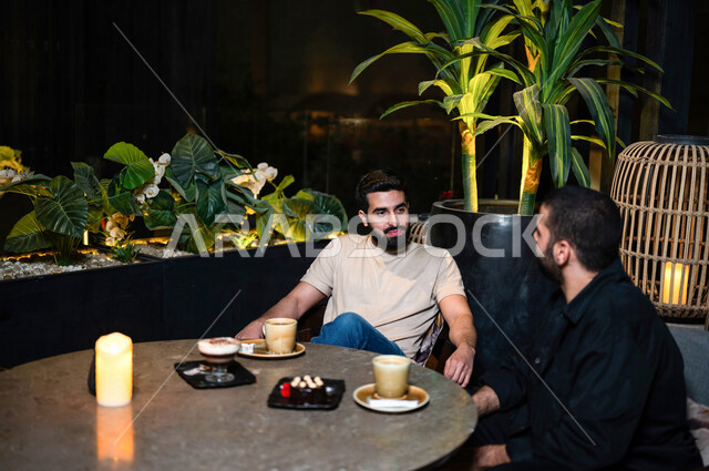شباب عرب خليجيون سعوديون يجلسون في احد مقاهي المملكة العربية السعودية، الاستمتاع بتبادل الحديث معاً، تناول القهوة والمشروبات الباردة والحلى اللذيذة، أجواء راقية، أنشطة شبابية ترفيهية، ايماءات وجه ويدين تدل على السعادة، الأجواء الشبابية في المقاهي السعودية