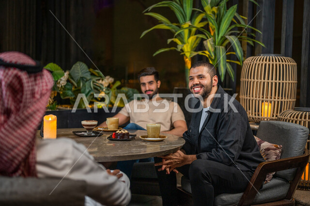 شباب عرب خليجيون سعوديون يجلسون في احد مقاهي المملكة العربية السعودية، الاستمتاع بتبادل الحديث معاً، تناول القهوة والمشروبات الباردة والحلى اللذيذة، أجواء راقية، أنشطة شبابية ترفيهية، ايماءات وجه ويدين تدل على السعادة، الأجواء الشبابية في المقاهي السعودية
