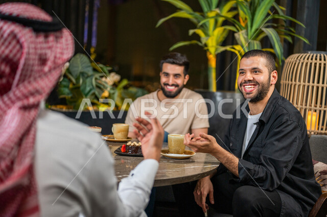 شباب عرب خليجيون سعوديون يجلسون في احد مقاهي المملكة العربية السعودية، الاستمتاع بتبادل الحديث معاً، تناول القهوة والمشروبات الباردة والحلى اللذيذة، أجواء راقية، أنشطة شبابية ترفيهية، ايماءات وجه ويدين تدل على السعادة، الأجواء الشبابية في المقاهي السعودية