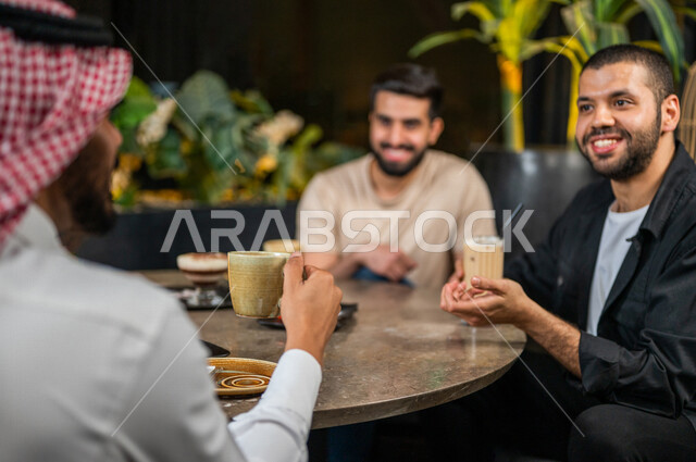 شباب عرب خليجيون سعوديون يجلسون في احد مقاهي المملكة العربية السعودية، الاستمتاع بتبادل الحديث معاً، تناول القهوة والمشروبات الباردة والحلى اللذيذة، أجواء راقية، أنشطة شبابية ترفيهية، ايماءات وجه ويدين تدل على السعادة، الأجواء الشبابية في المقاهي السعودية