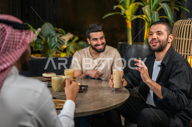 شباب عرب خليجيون سعوديون يجلسون في احد مقاهي المملكة العربية السعودية، الاستمتاع بتبادل الحديث معاً، تناول القهوة والمشروبات الباردة والحلى اللذيذة، أجواء راقية، أنشطة شبابية ترفيهية، ايماءات وجه ويدين تدل على السعادة، الأجواء الشبابية في المقاهي السعودية