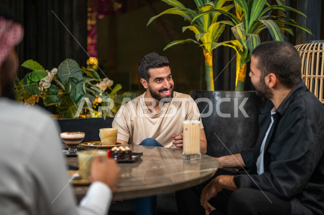 شباب عرب خليجيون سعوديون يجلسون في احد مقاهي المملكة العربية السعودية، الاستمتاع بتبادل الحديث معاً، تناول القهوة والمشروبات الباردة والحلى اللذيذة، أجواء راقية، أنشطة شبابية ترفيهية، ايماءات وجه ويدين تدل على السعادة، الأجواء الشبابية في المقاهي السعودية