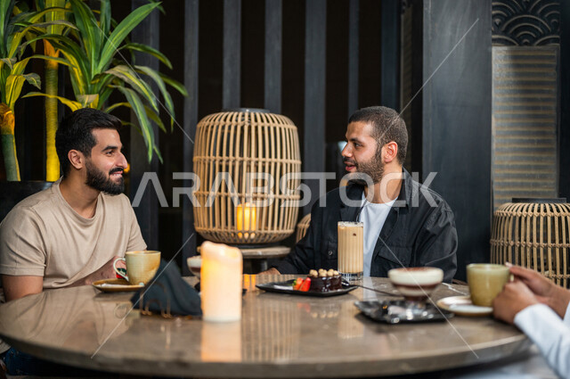 شباب عرب خليجيون سعوديون يجلسون في احد مقاهي المملكة العربية السعودية، الاستمتاع بتبادل الحديث معاً، تناول القهوة والمشروبات الباردة والحلى اللذيذة، أجواء راقية، أنشطة شبابية ترفيهية، ايماءات وجه ويدين تدل على السعادة، الأجواء الشبابية في المقاهي السعودية