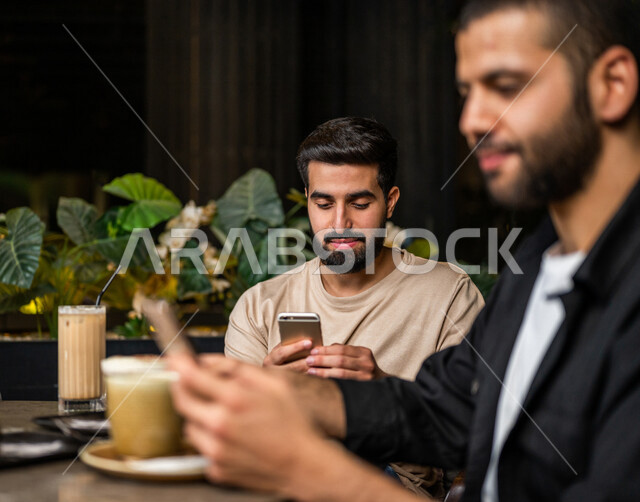 شباب عرب خليجيون سعوديون يجلسون في احد مقاهي المملكة العربية السعودية، استخدام جهاز الهاتف المحمول، تناول القهوة والمشروبات الباردة والحلى اللذيذة، أجواء راقية، أنشطة شبابية ترفيهية، الأجواء الشبابية في المقاهي السعودية