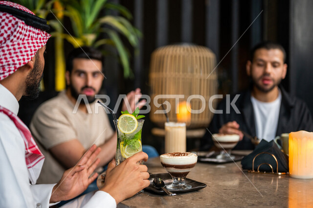 شباب عرب خليجيون سعوديون يجلسون في احد مقاهي المملكة العربية السعودية، الاستمتاع بتبادل الحديث معاً، تناول القهوة والمشروبات الباردة والحلى اللذيذة، أجواء راقية، أنشطة شبابية ترفيهية، ايماءات وجه ويدين تدل على السعادة، الأجواء الشبابية في المقاهي السعودية