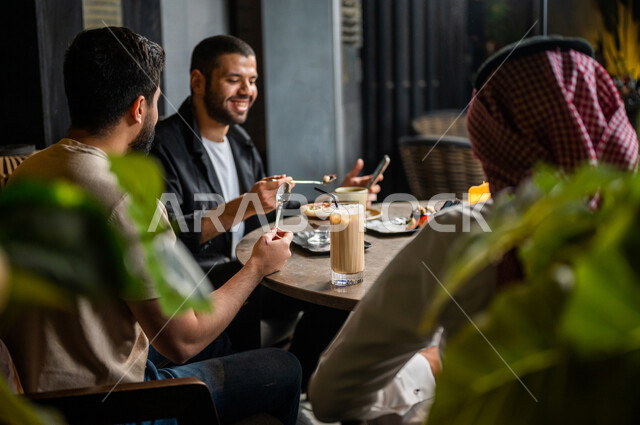 شباب عرب خليجيون سعوديون يجلسون في احد مقاهي المملكة العربية السعودية، الاستمتاع بتبادل الحديث معاً، تناول القهوة والمشروبات الباردة والحلى اللذيذة، أجواء راقية، أنشطة شبابية ترفيهية، ايماءات وجه ويدين تدل على السعادة، الأجواء الشبابية في المقاهي السعودية