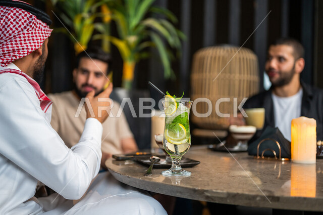 شباب عرب خليجيون سعوديون يجلسون في احد مقاهي المملكة العربية السعودية، الاستمتاع بتبادل الحديث معاً، تناول القهوة والمشروبات الباردة والحلى اللذيذة، أجواء راقية، أنشطة شبابية ترفيهية، ايماءات وجه ويدين تدل على السعادة، الأجواء الشبابية في المقاهي السعودية