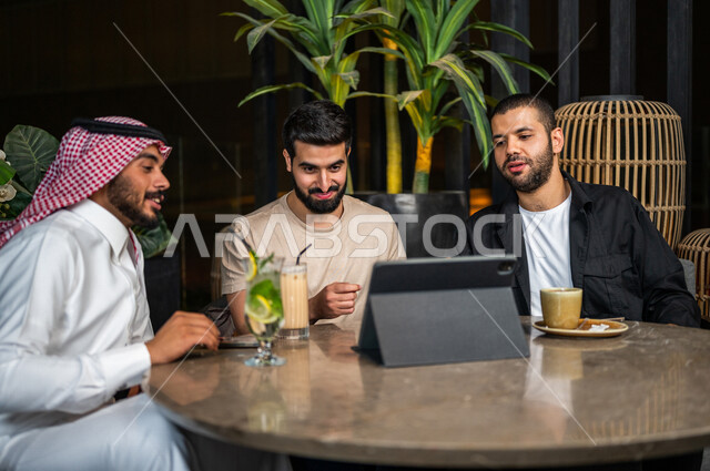 شباب عرب خليجيون سعوديون يجلسون في احد مقاهي المملكة العربية السعودية، الاستمتاع بمشاهدة البرامج الترفيهية من خلال التابليت المحمول، مباريات رياضية، إيماءات وجه و يدين تدل على السعادة، أنشطة شبابية ترفيهية، الأجواء الشبابية في المقاهي السعودية